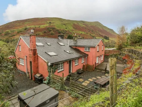Cottage with slate roof and patio, set against hillside with stone wall fencing