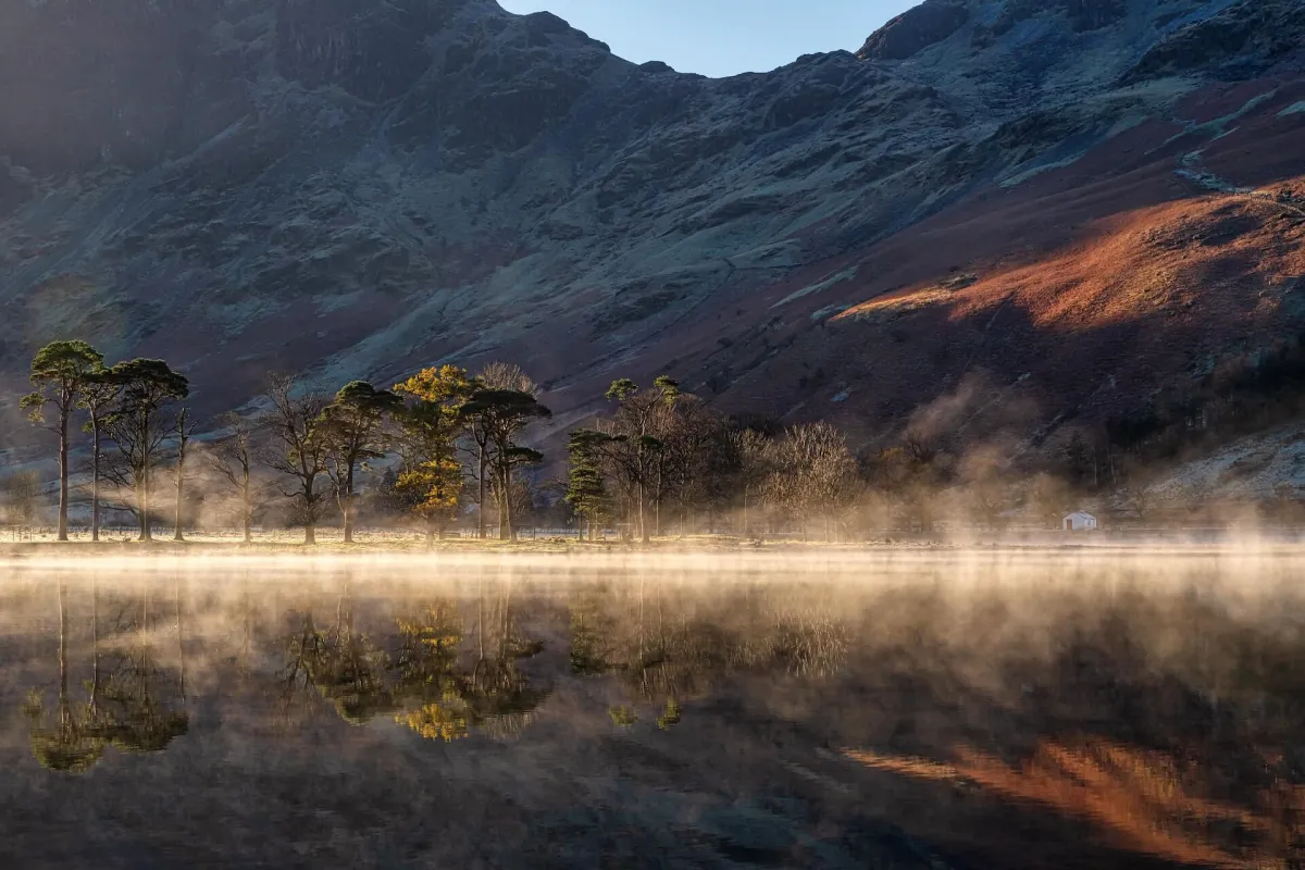 Misty morning on a calm Lake District water with trees reflected in the surface, creating a peaceful and romantic atmosphere.
